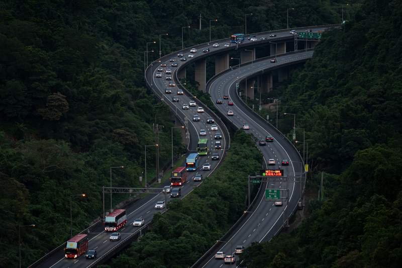 空拍蜿蜒於山區綠林間的高速公路車流，象徵現代城市運輸系統在自然環境中的延伸，以及推動電動交通減排實踐對生態與公共健康的必要性。